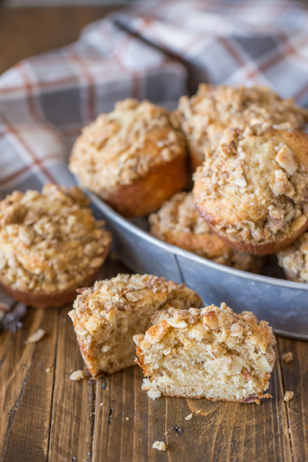 A Banana Muffin With Almond Oat Streusel Topping cut in half, with a galvanized bowl of muffins in the background.  