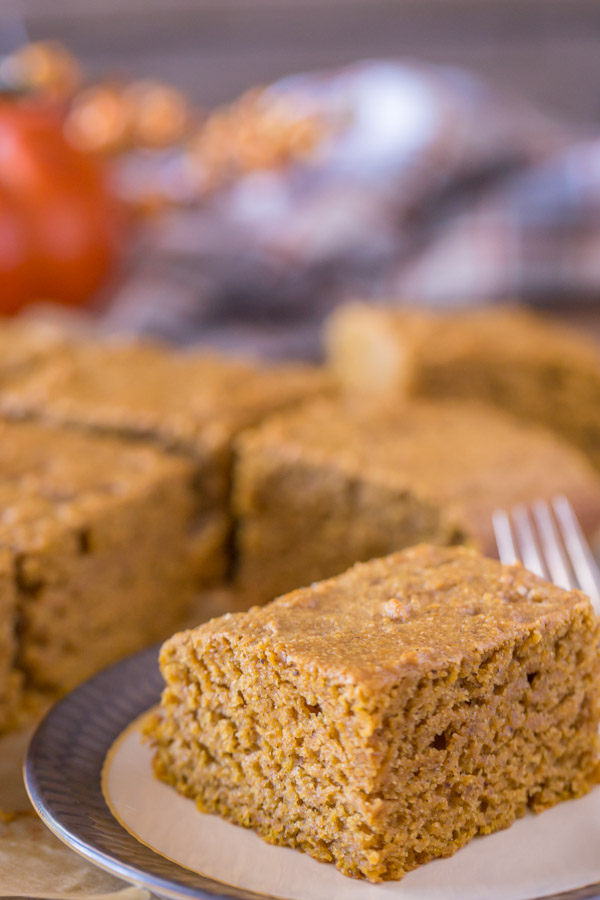 A piece of Healthier Pumpkin Spice Snack Cake on a plate, with more of the cake in the background.  