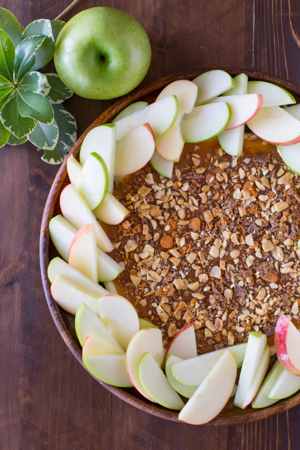 Easy Caramel Apple Dip on a wood plate with sliced apples arranged around it, and a whole apple sitting next to it.  