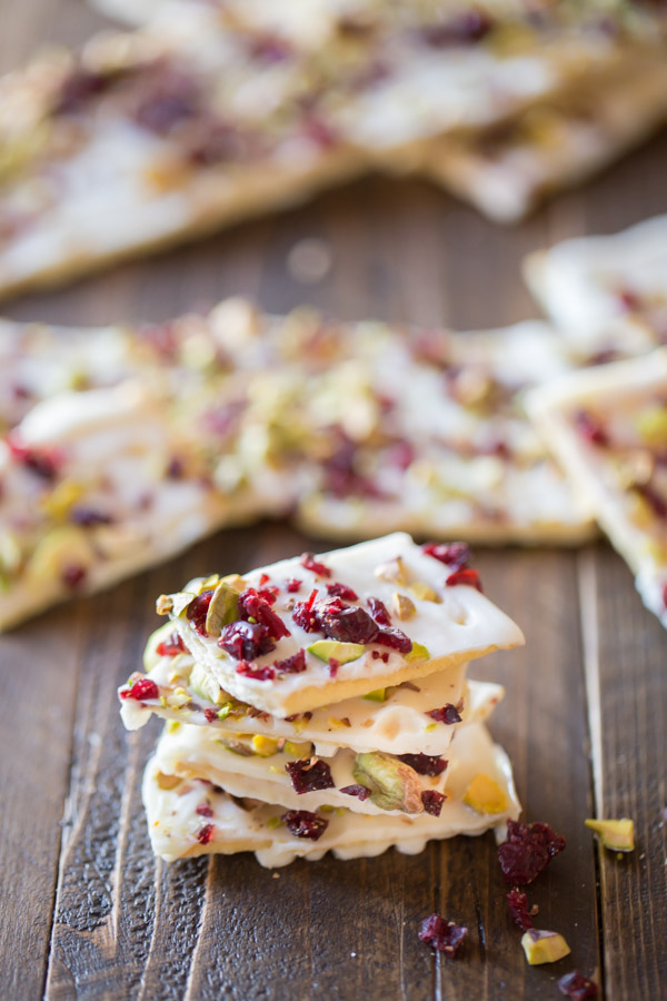 A few pieces of Cranberry Pistachio Butter Cracker Bark stacked, with more Cranberry Pistachio Butter Cracker Bark in the background. 