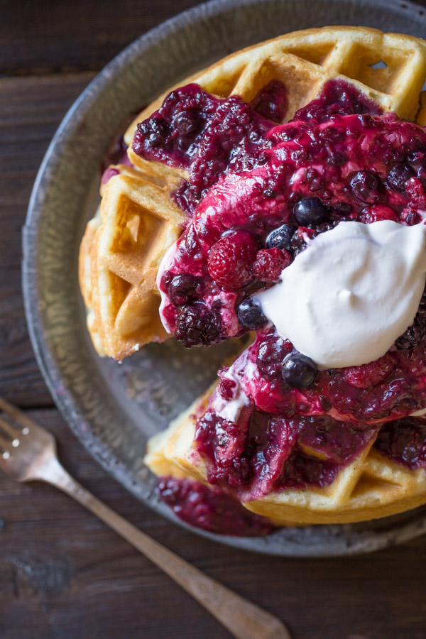 Best Ever Buttermilk Waffles on a plate, topped with berry sauce, whole berries and whipped cream.  