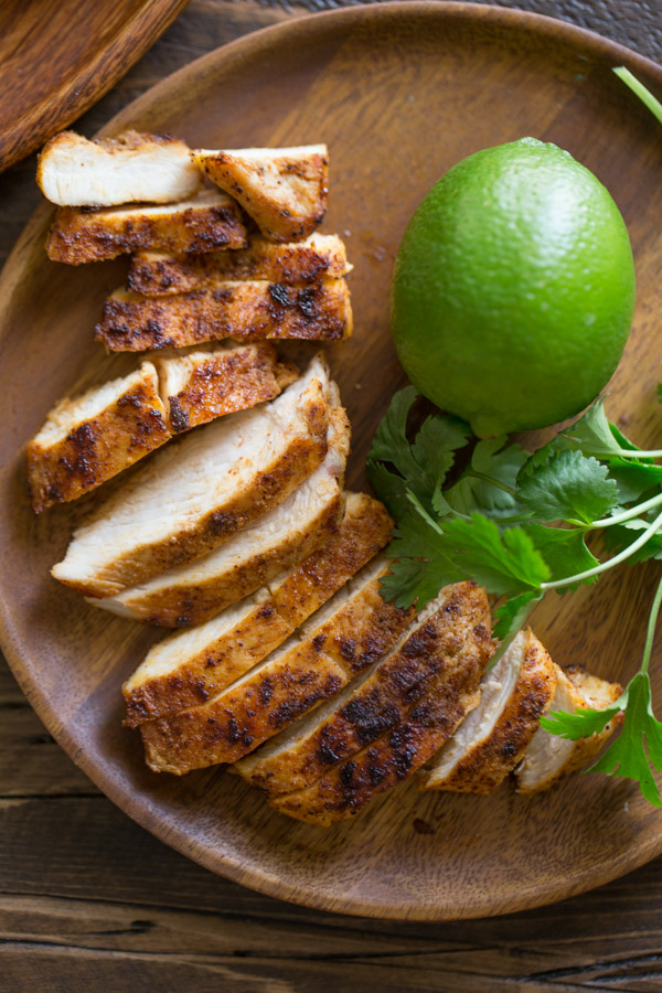 A wood plate with the sliced grilled chicken for the Green Chile Chicken Waffletada, along with a whole lime and some cilantro. 