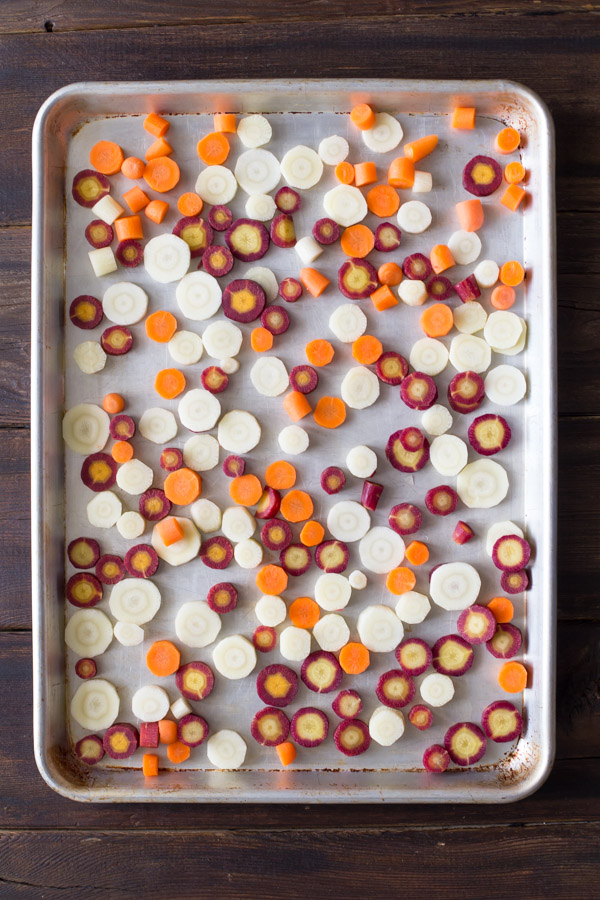 Purple, white and orange carrot slices on a baking sheet before roasting.  