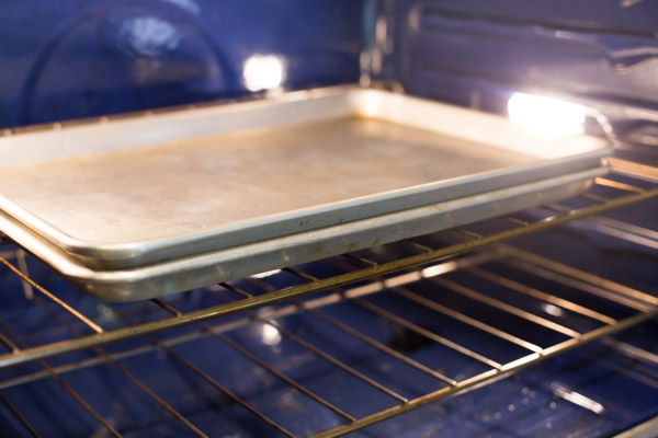 A baking sheet with carrots on it, with another baking sheet on top of the carrots in the oven for roasting. 