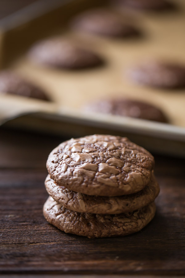 A stack of three Soft and Chewy Brownie Cookies, with more cookies on a parchment paper lined baking sheet in the background. 