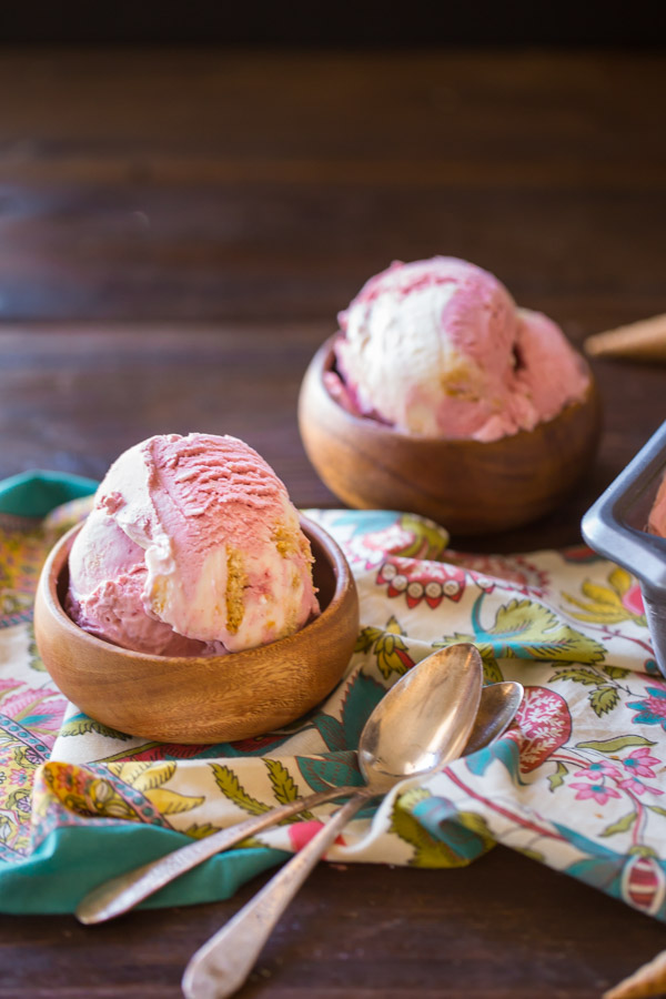 Homemade Raspberry Cheesecake Ice Cream in two small wood bowls with two spoons next to the bowl in front.  