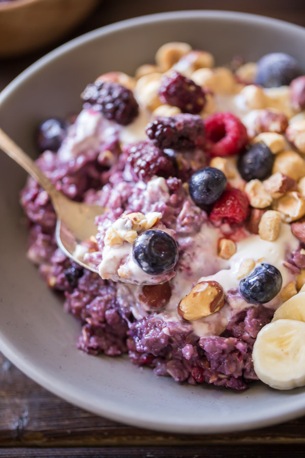 Triple Berry Oatmeal Breakfast Bowl topped with vanilla yogurt, crushed hazelnuts, sliced banana, and berries.