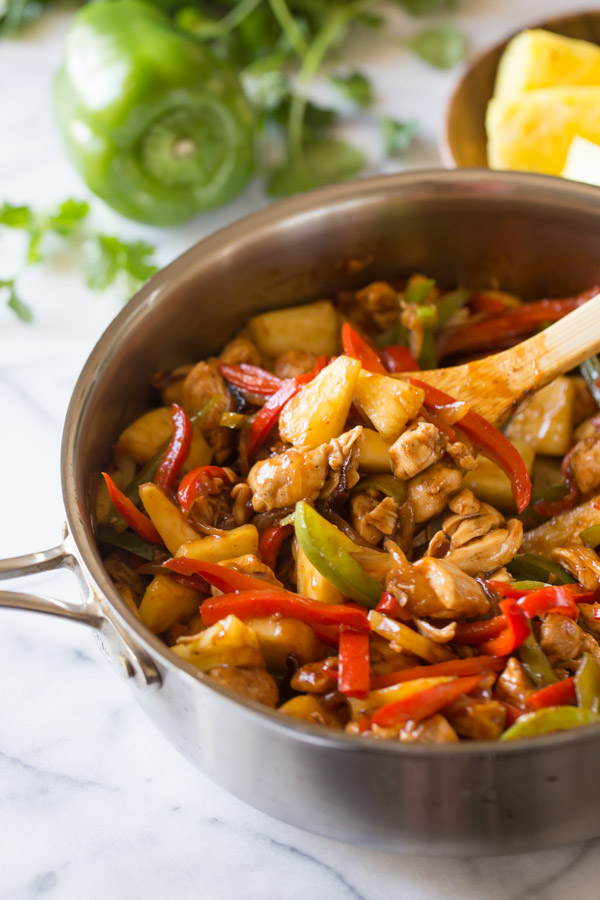 BBQ Chicken Fajitas in a large skillet with a wooden spoon in it, and a whole green paper and pineapple chunks in the background.
