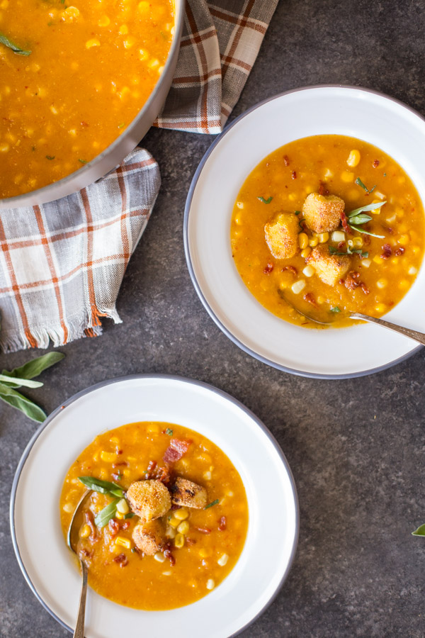 Two bowls of Butternut Squash Corn Chowder with Goat Cheese Croutons on top, sitting next to a large pot of Butternut Squash Corn Chowder.