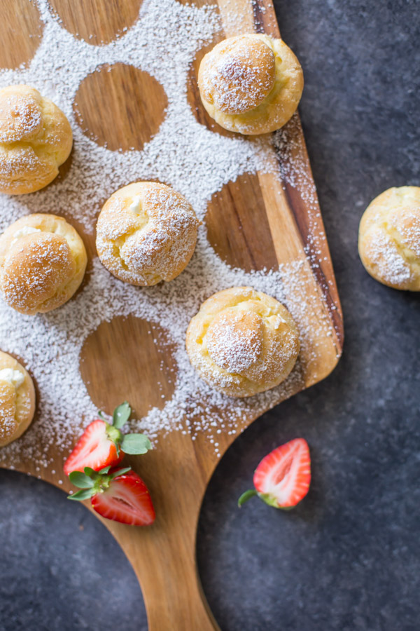 Classic Cream Puffs dusted with powdered sugar, sitting on a cutting board.