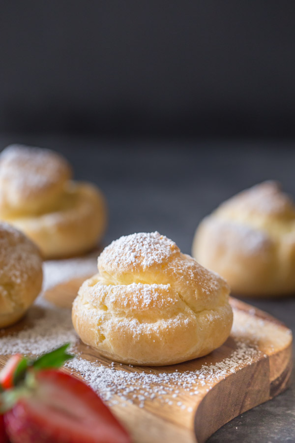 Classic Cream Puffs dusted with powdered sugar, sitting on a cutting board.