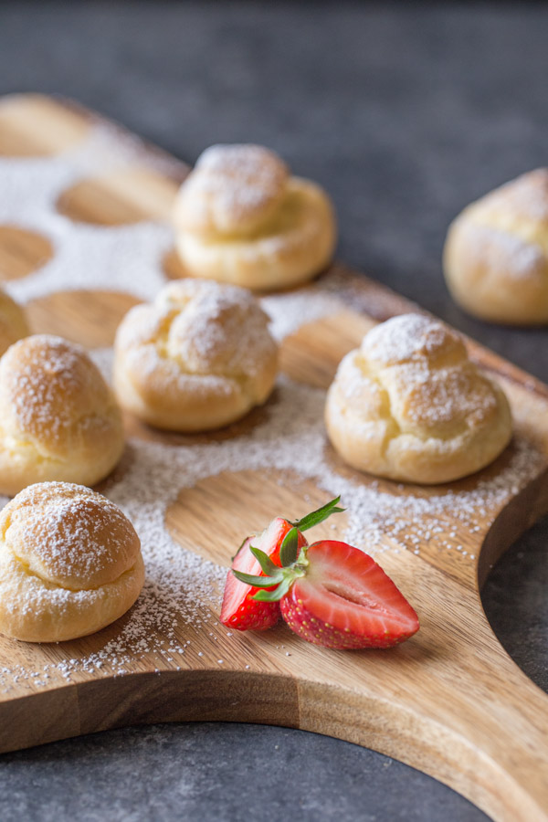 Classic Cream Puffs dusted with powdered sugar, sitting on a cutting board.