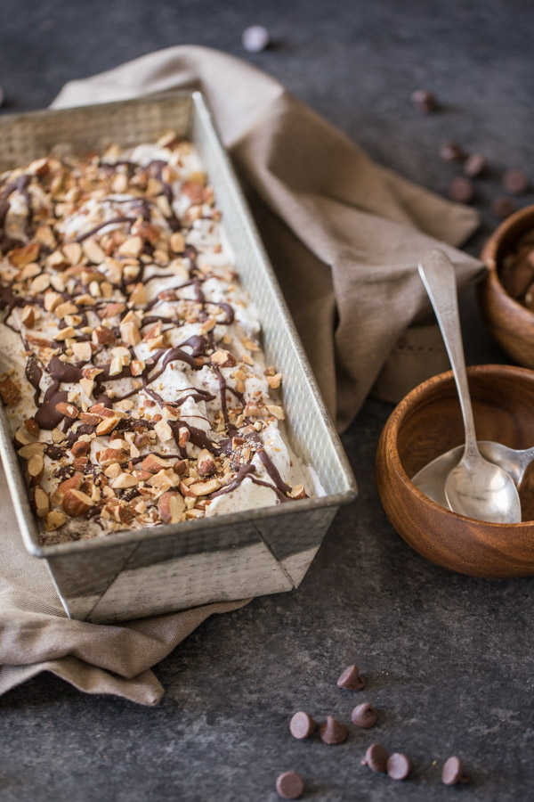 Dark Chocolate Almond Ice Cream in a loaf pan, sitting next to a small wood bowl with two spoons in it. 