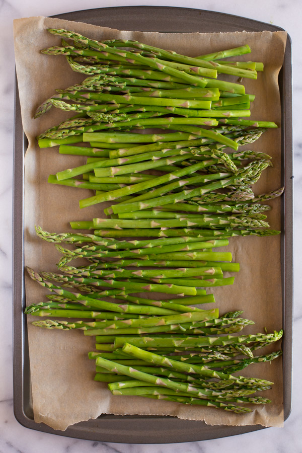Trimmed asparagus on a parchment paper lined baking sheet. 