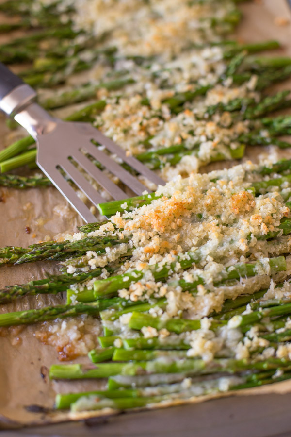 Roasted Asparagus With Panko and Gruyere on a parchment paper lined baking sheet with a spatula. 