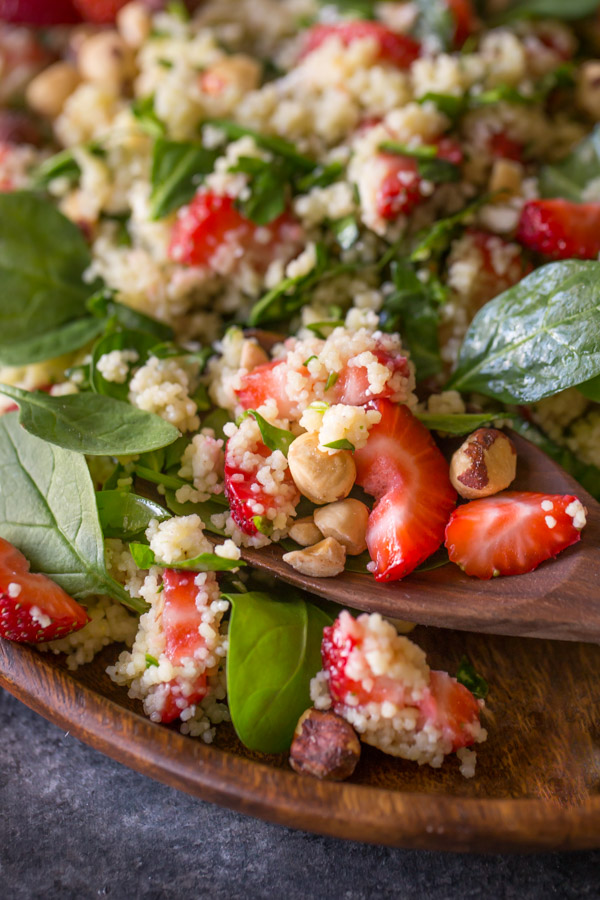Strawberry Couscous Spinach Salad on a wood plate with a wooden spoon in it.  