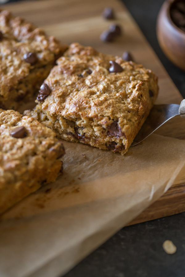 Whole Wheat Oatmeal Chocolate Chip Snack Bars on parchment paper sitting on a board, and a spatula under one of the bars.