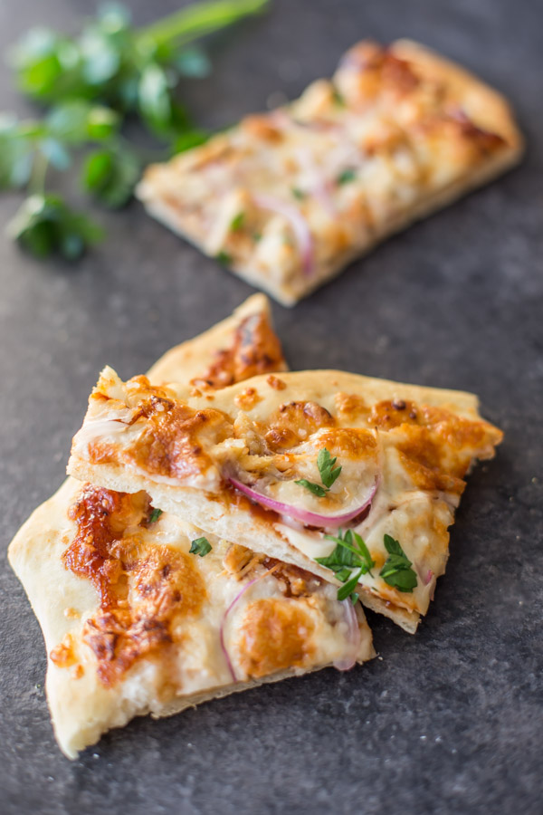 Two slices of Barbeque Chicken Pizza, with another slice in the the background next to some flat leaf parsley.