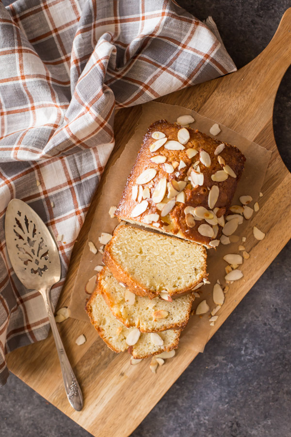 Glazed Almond Poppy Seed Bread sliced on a wood cutting board with a serving spatula next to it. 