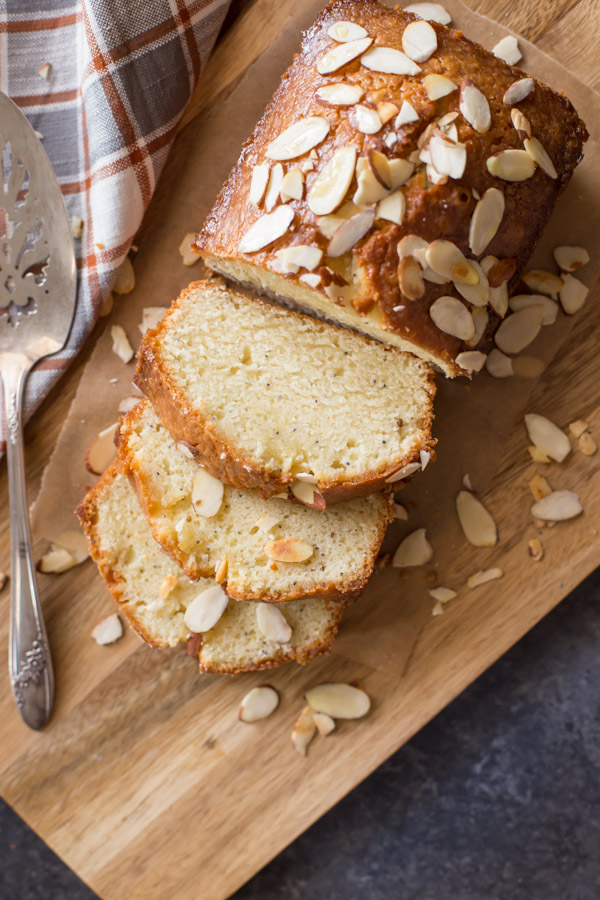 Glazed Almond Poppy Seed Bread sliced on a wood cutting board with a serving spatula next to it. 