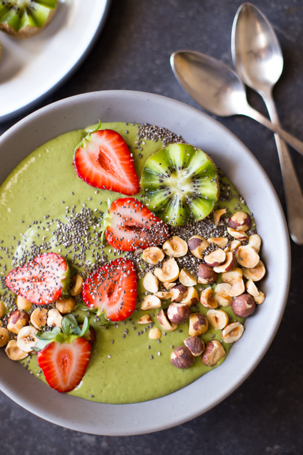 Strawberry Kiwi Protein Smoothie Bowl topped with sliced fresh strawberries and kiwi, hazelnuts, and chia seeds, with two spoons next to the bowl.