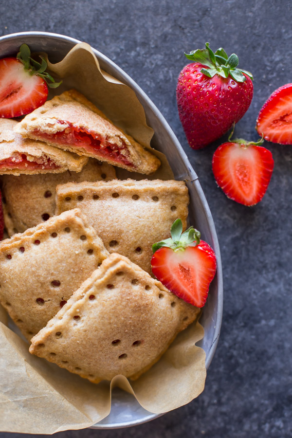 Whole Wheat Strawberry Rhubarb Fruit Pockets in a metal bowl, with some fresh strawberries in the bowl and next to it.  