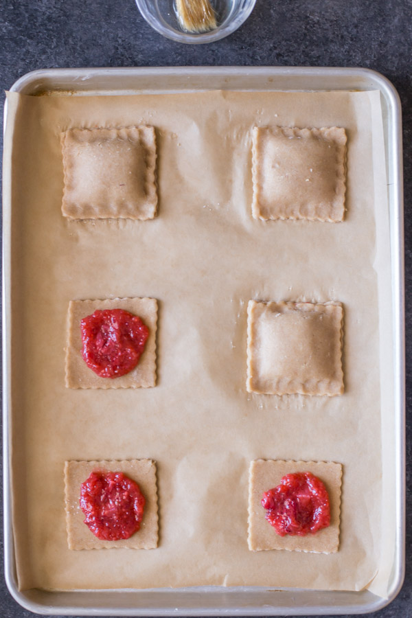 Whole Wheat Strawberry Rhubarb Fruit Pockets being assembled on a parchment paper lined baking sheet. 