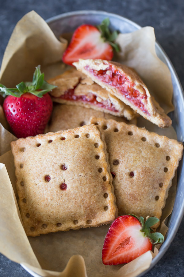 Whole Wheat Strawberry Rhubarb Fruit Pockets in a metal bowl, with some fresh strawberries. 
