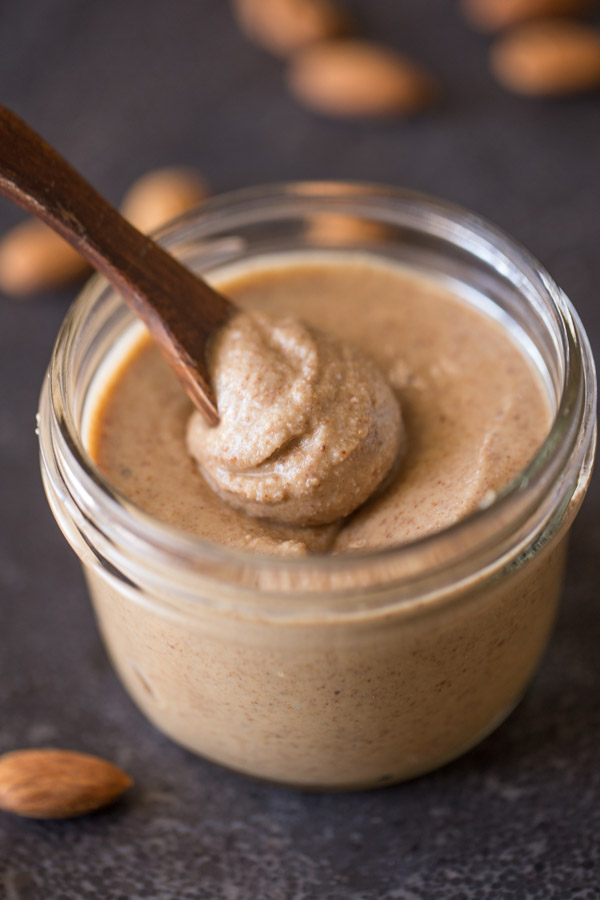A small glass jar of Homemade Almond Butter with a small wood spoon in it.  
