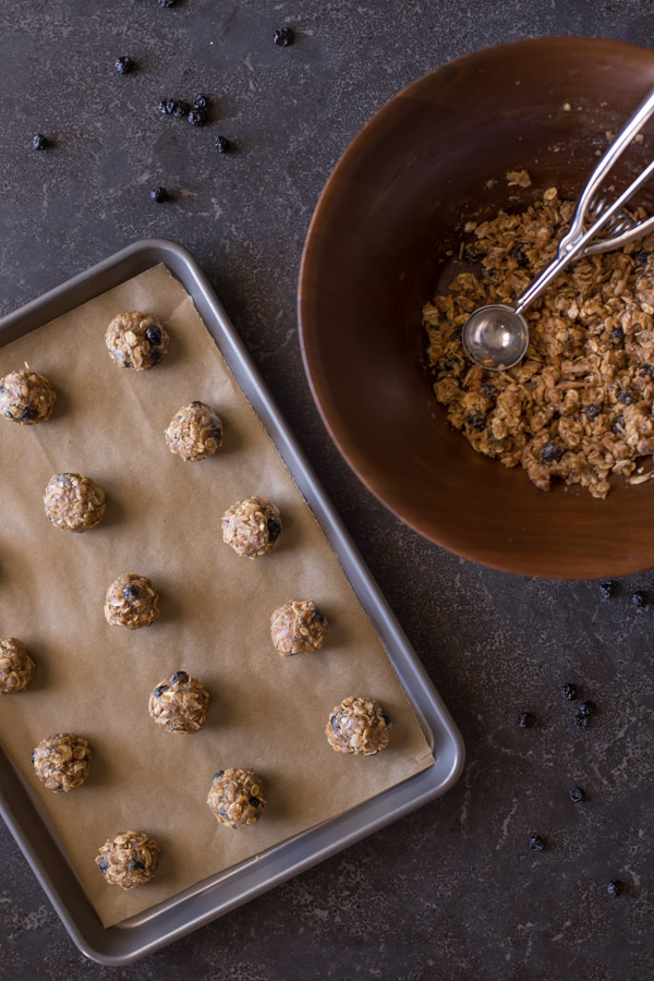 Blueberry Muffin Energy Bites on a parchment paper lined baking sheet, with the bowl of the mixed ingredients sitting next to it with a cookie dough scoop in it. 