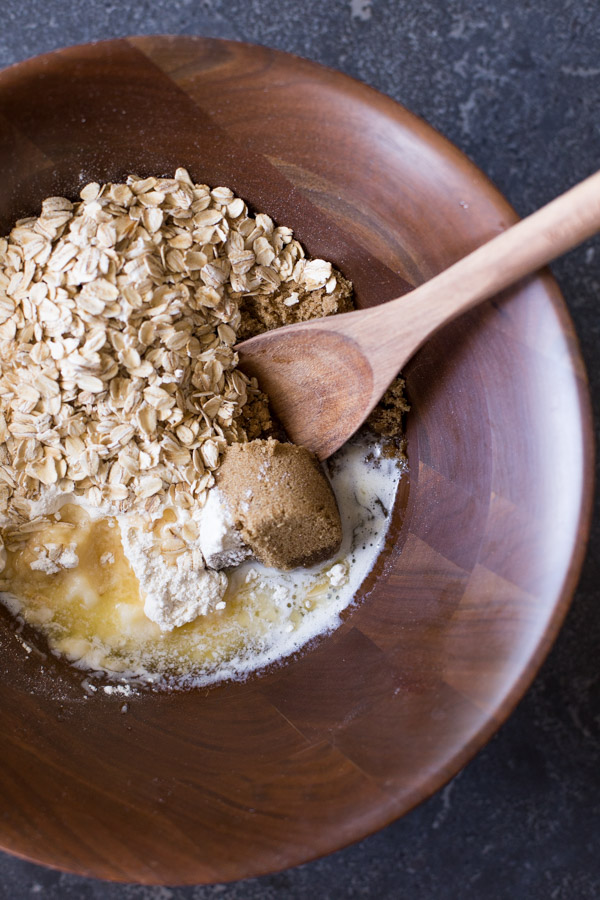 A wood bowl of the melted butter, brown sugar, flour, oats, and baking soda, with a wooden spoon in it. 