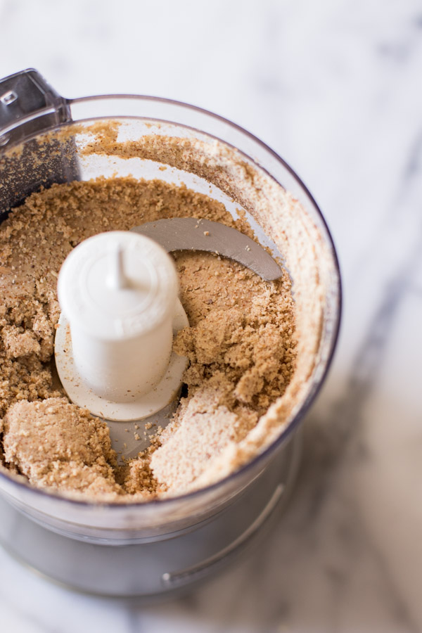 A food processor with the almonds being pureed.  