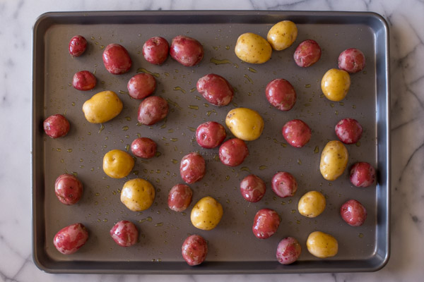 A baking sheet with potatoes coated with olive oil and seasoned with salt and pepper.