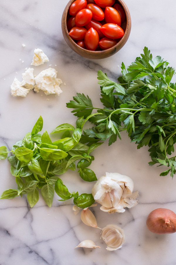 A small wood bowl of grape tomatoes, feta cheese, fresh herbs and garlic bulbs. 