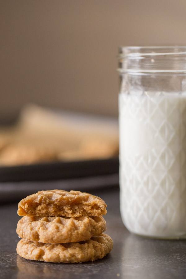 A half of a Small Batch Peanut Butter Cookie sitting on top of two whole cookies, with a glass of milk next to them.