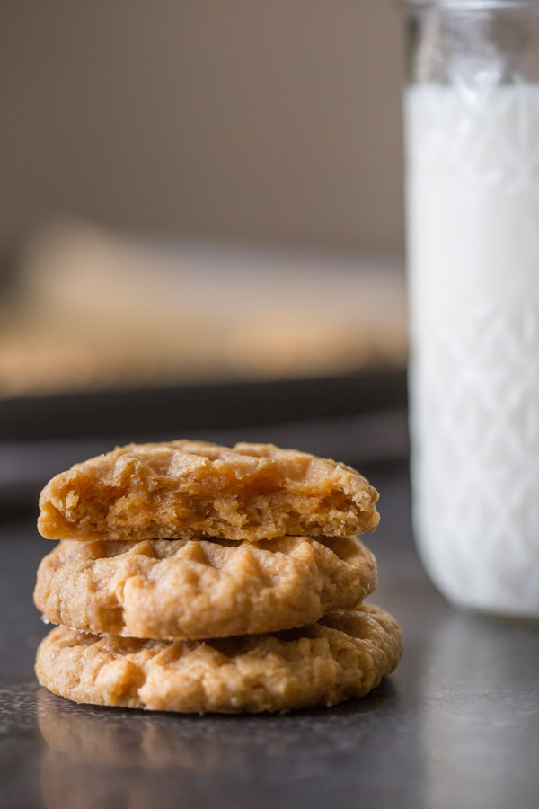 A half of a Small Batch Peanut Butter Cookie sitting on top of two whole cookies, and a glass of milk in the background. 