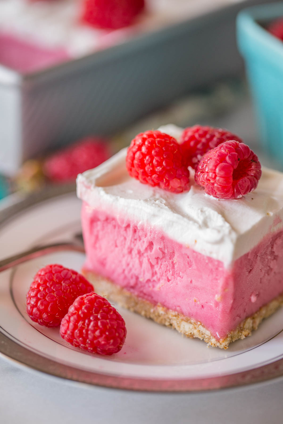 A piece of Cool and Creamy Raspberry Pretzel Dessert on a plate with fresh raspberries. 