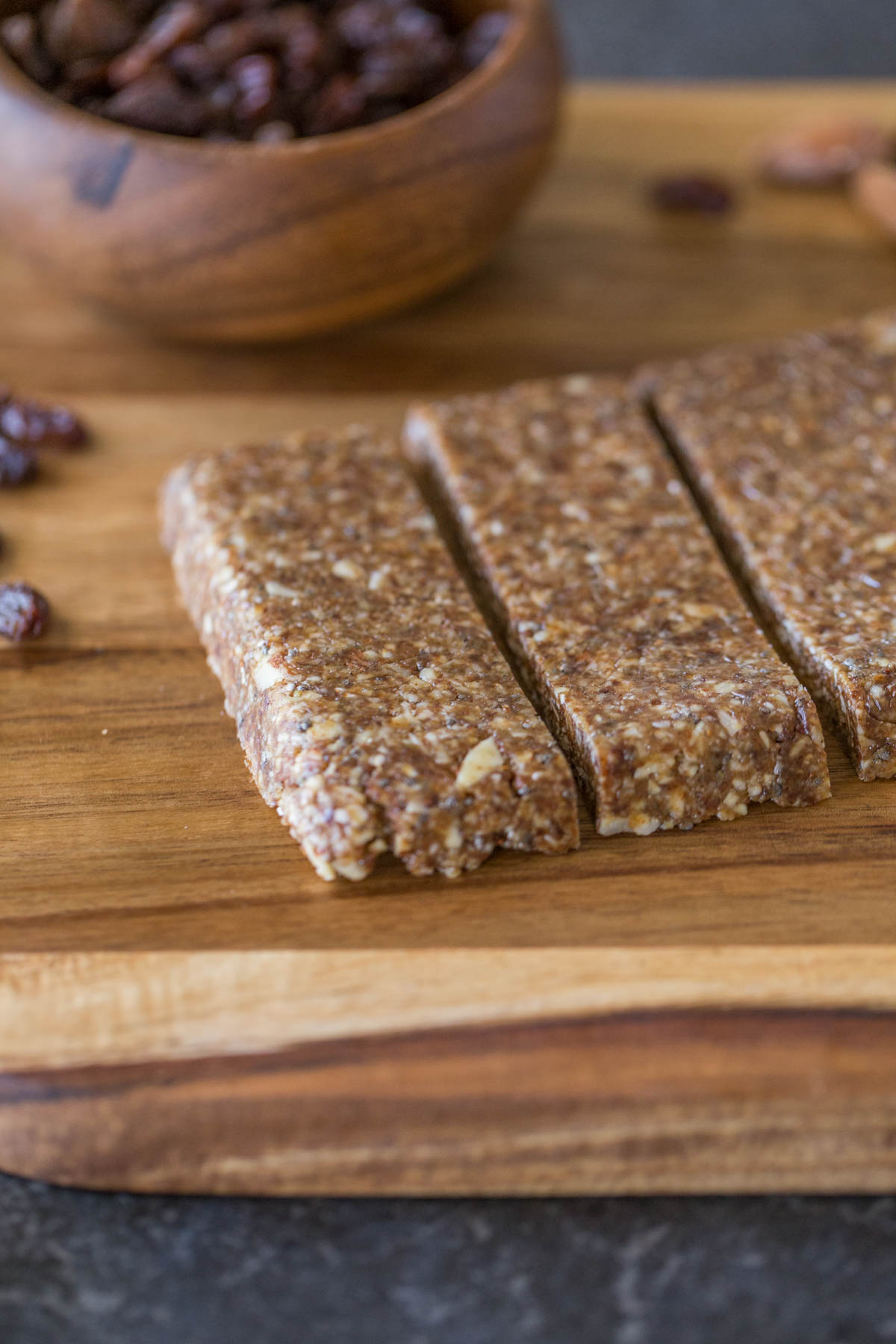 Five Ingredient No Bake Energy Bars on a cutting board, along with a small wood bowl of raisins. 