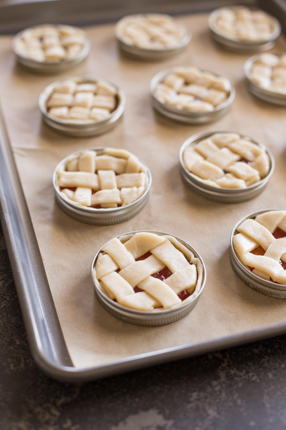 Mini Mason Jar Lid Strawberry Pies assembled and arranged on a parchment paper lined baking sheet before baking. 