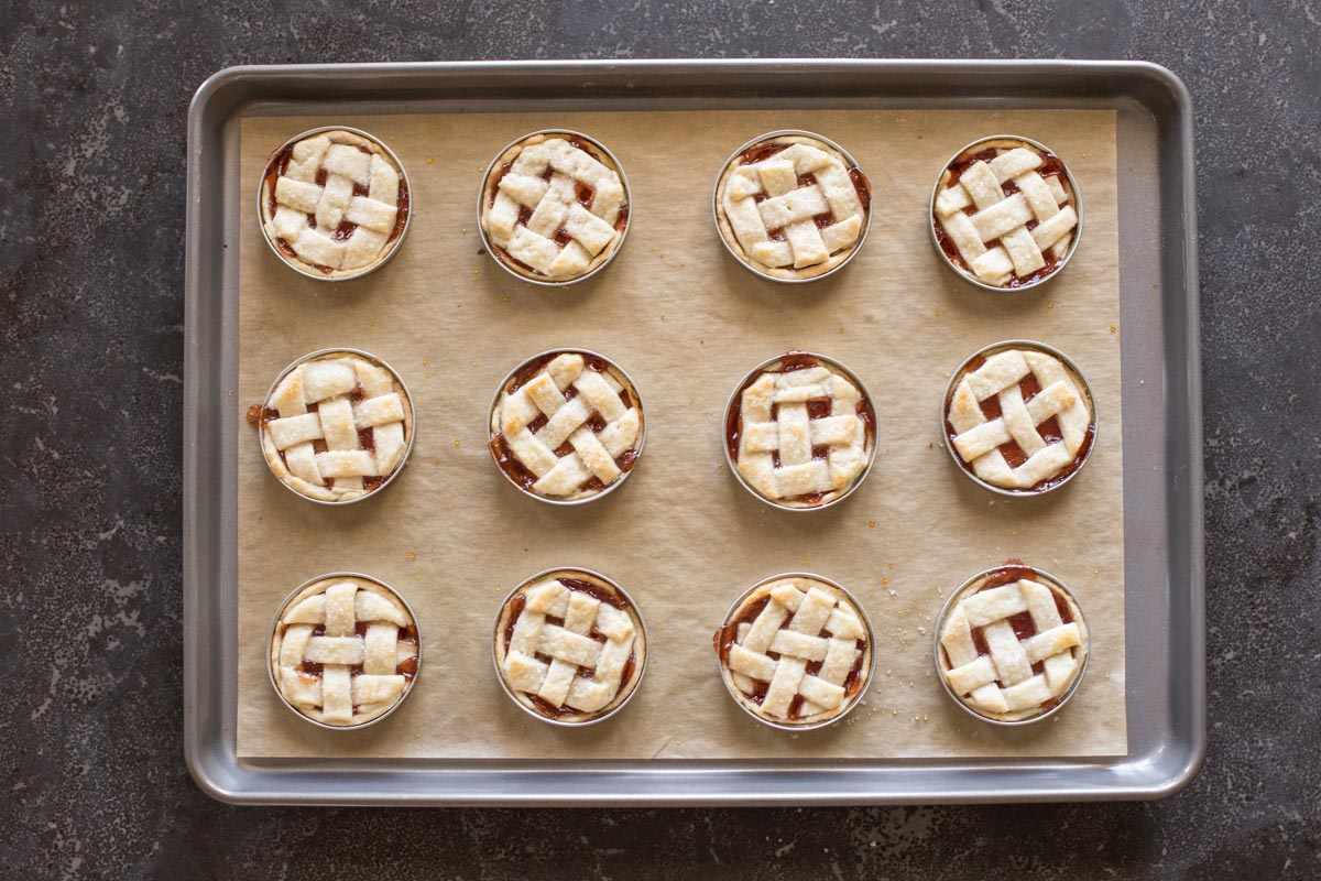 Mini Mason Jar Strawberry Pies on a parchment paper lined baking sheet after they have been baked. 