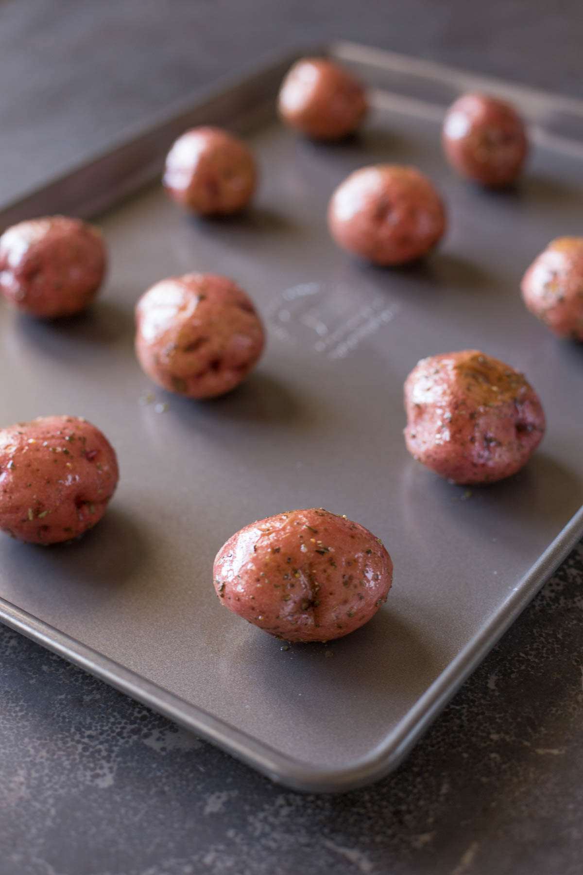 Whole red potatoes coated in olive oil, salt and pepper, arranged on a baking sheet. 