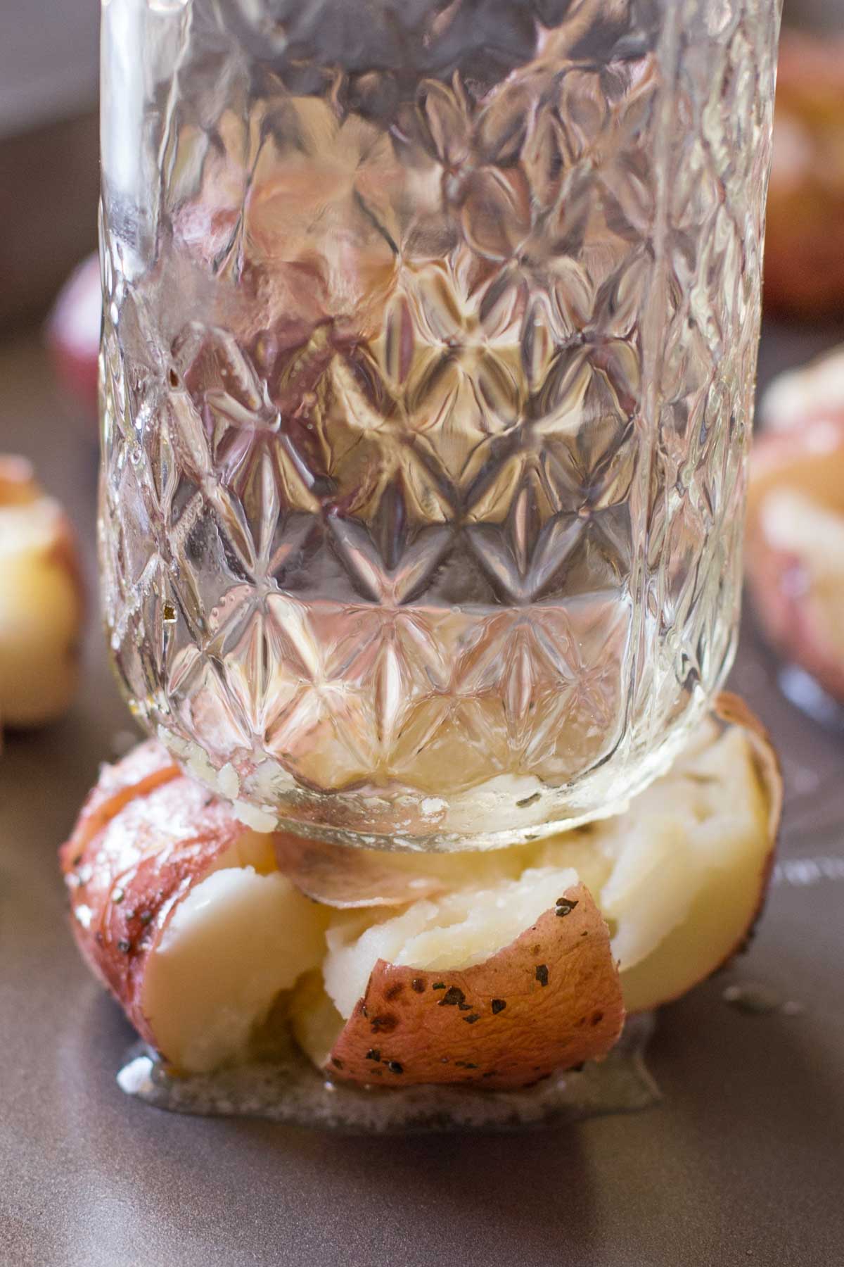 A bottom of a glass being used to smash the roasted potato.  