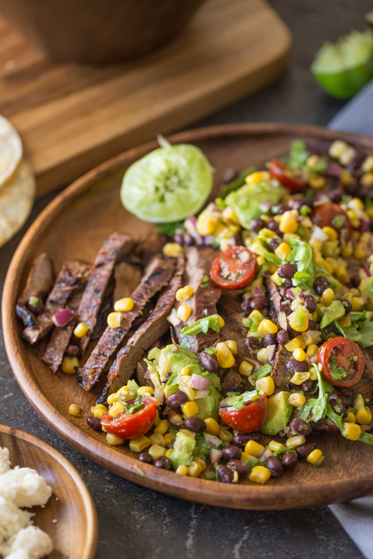 A large wood plate of sliced grilled marinated flank steak and avocado salad.