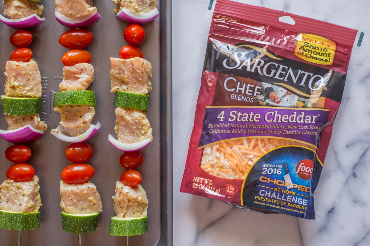 Pork Tenderloin Kabobs on a baking sheet before being grilled, with a package of Sargento® Chef Blends 4 State Cheddar next to the baking sheet. 