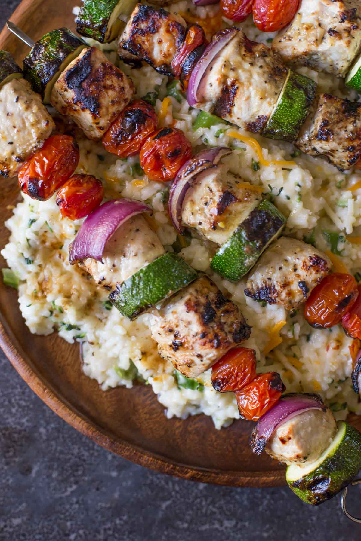 Pork Tenderloin Kabobs served over Cheesy Broccoli Rice on a large wood plate.