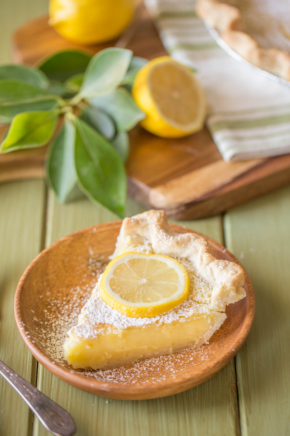 A slice of Whole Lemon Pie dusted with powdered sugar and topped with a lemon slice, on a plate. 