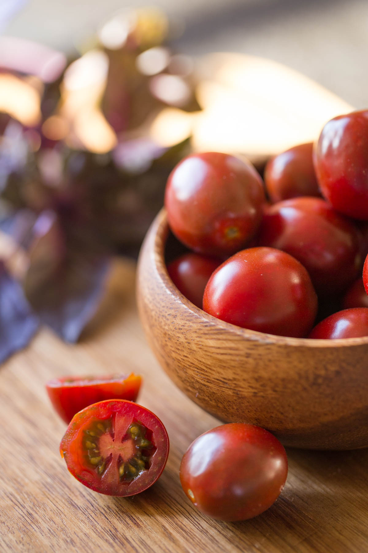 A small wood bowl of grape tomatoes, with a few tomatoes sitting next to the bowl. 