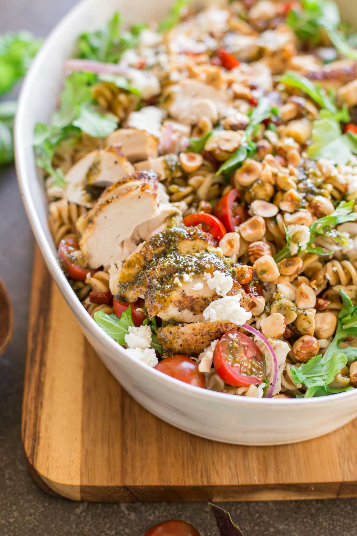 Whole Wheat Pasta Salad With Honey Basil Balsamic Vinaigrette in a large serving bowl, sitting on a cutting board. 