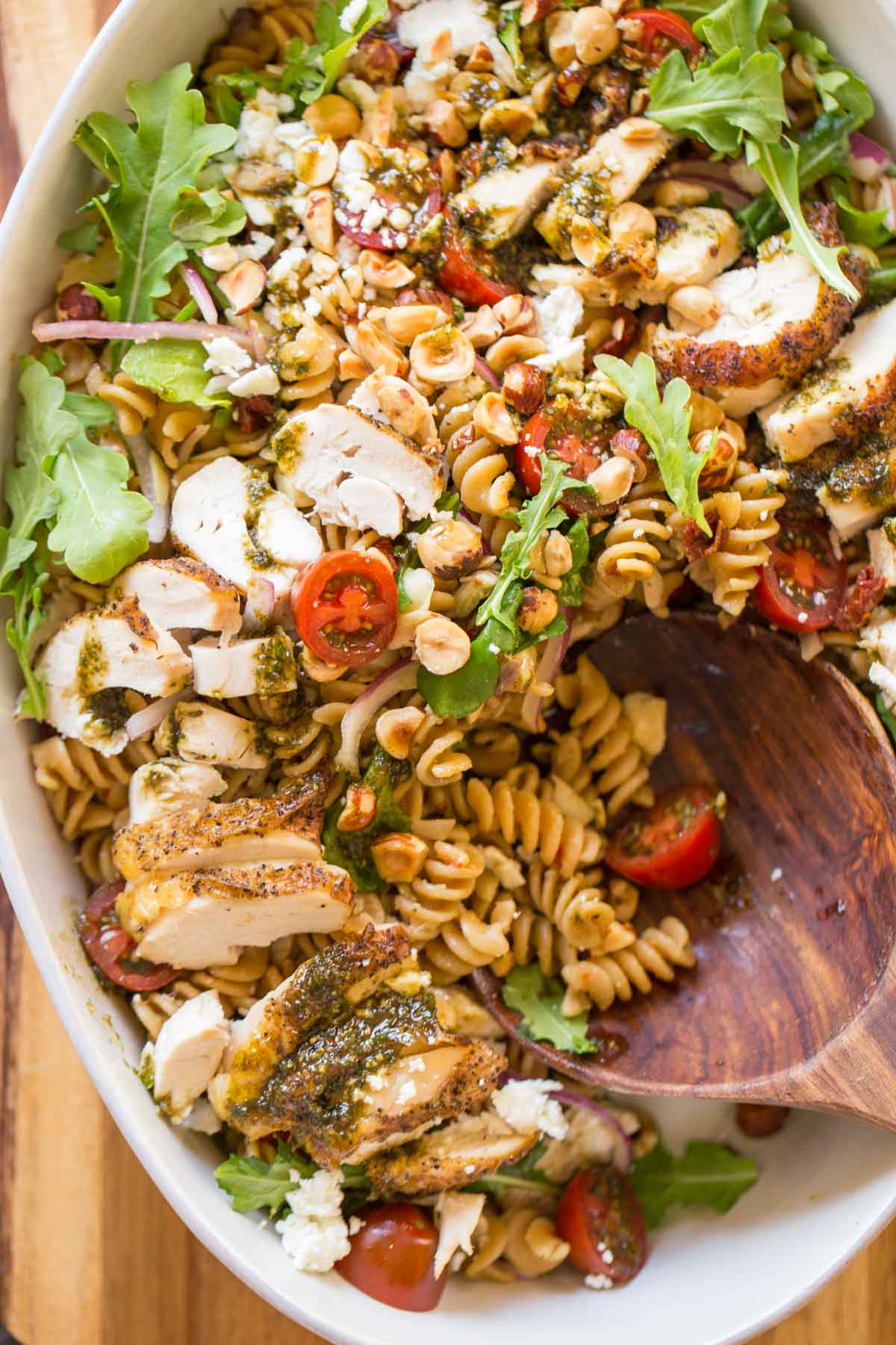 Whole Wheat Pasta Salad With Honey Basil Balsamic Vinaigrette in a large serving bowl with a wooden spoon in it.