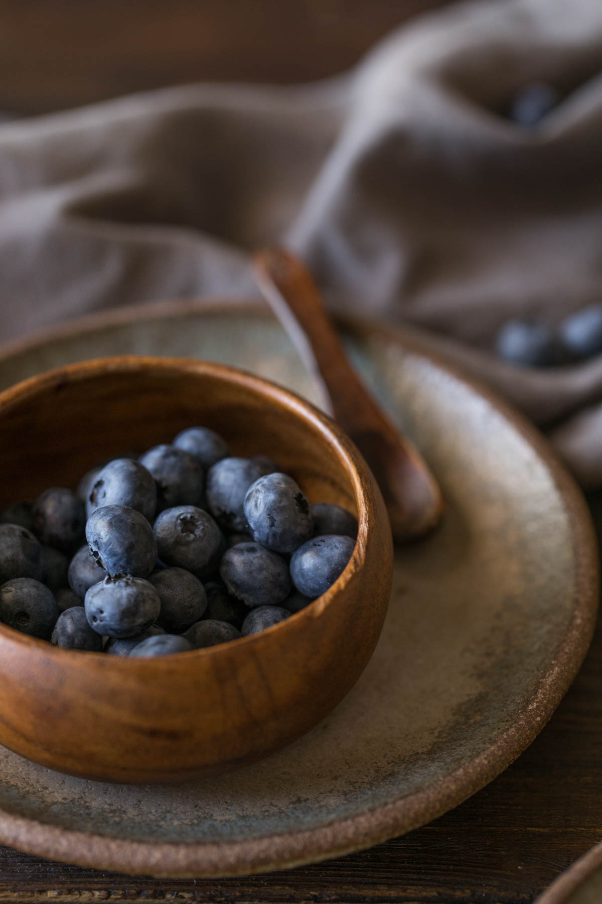 A small wood bowl of blueberries sitting on a plate with a small wooden spoon. 